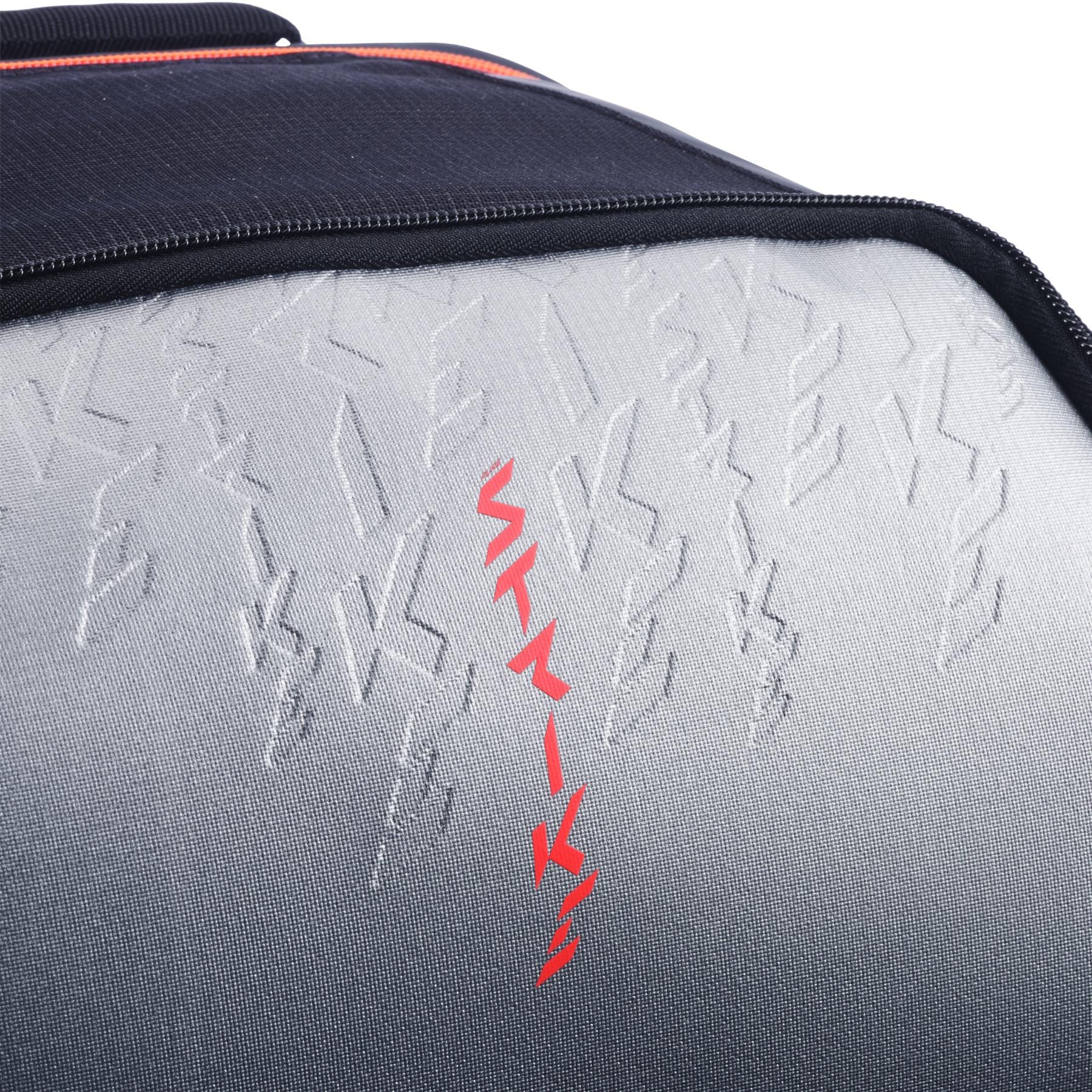 Close-up of the textured gray and black surface on the Babolat Pure Strike Tennis Backpack - Carbon Grey by Babolat, featuring embossed zigzag patterns and a bold vertical line of red zigzag shapes in the center.