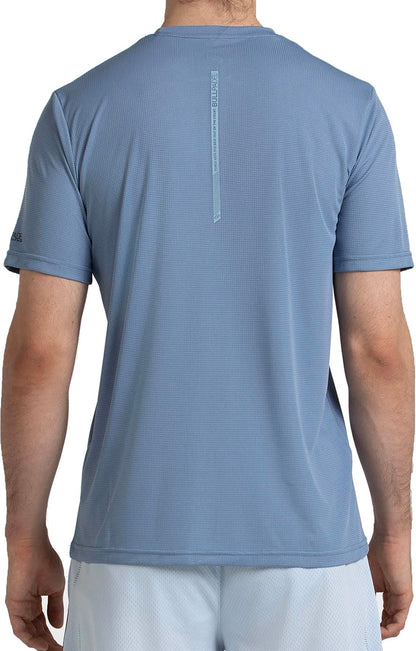 A man is seen from behind wearing a Bullpadel Cabore Mens Padel T-Shirt in Shadow Blue, featuring Quickerdry technology and a vertical Bullpadel logo below the back neckline, paired with white shorts.