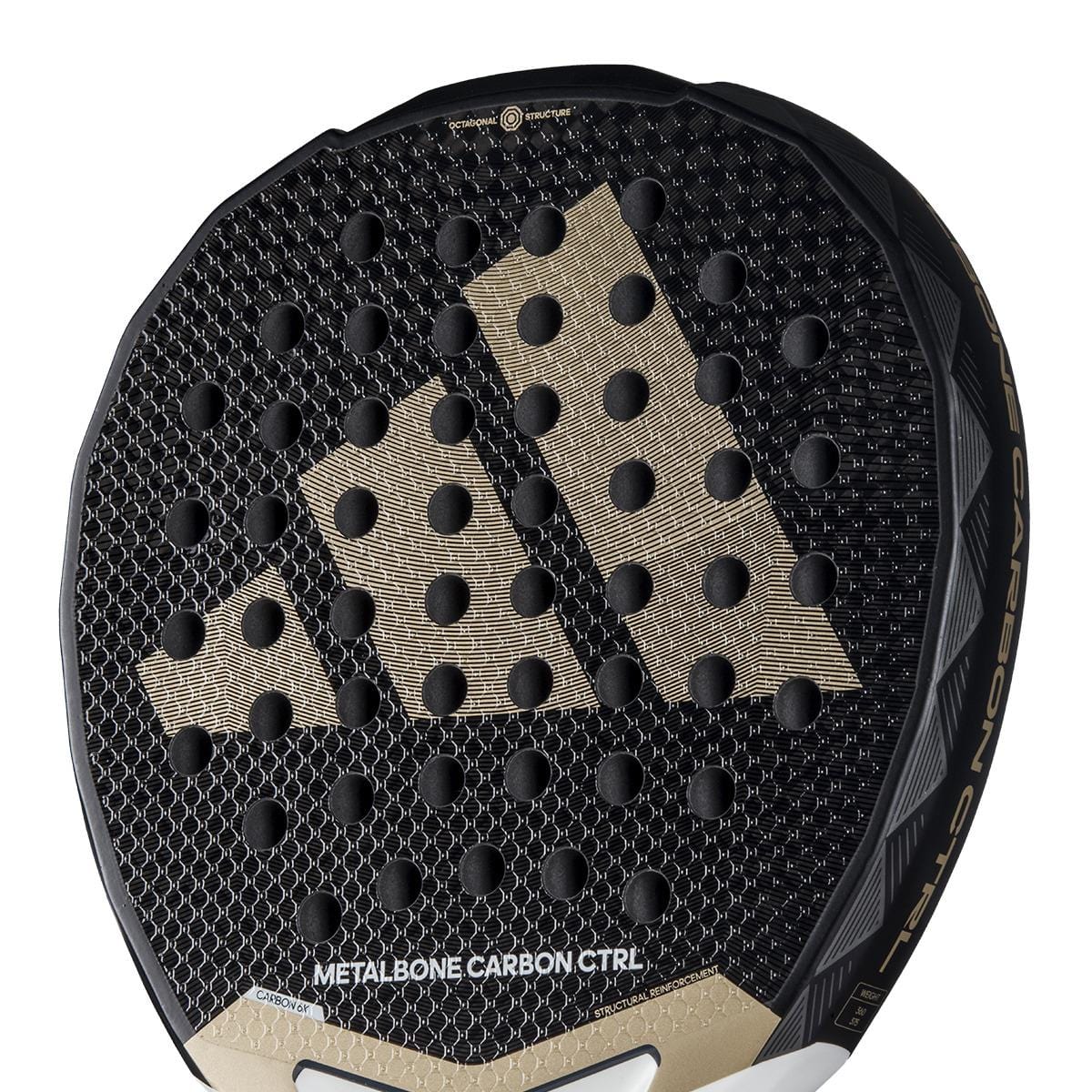 Close-up of the adidas Metalbone Carbon CTRL 3.4 padel racket for advanced players, with a gold adidas logo, circular perforations, and "METALBONE CARBON CTRL" on the lower section.