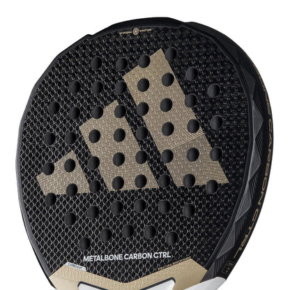 Close-up of the adidas Metalbone Carbon CTRL 3.4 padel racket for advanced players, with a gold adidas logo, circular perforations, and "METALBONE CARBON CTRL" on the lower section.