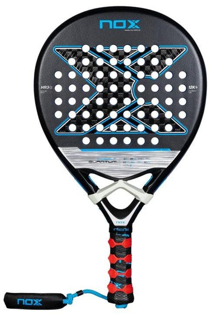The NOX Luxury Quantum 12K Cobalt 2025 Padel Racket features a black frame with blue and white accents, a large "X" on the face, premium 12K carbon fiber, and a decorated handle with black-red grip and wrist strap.