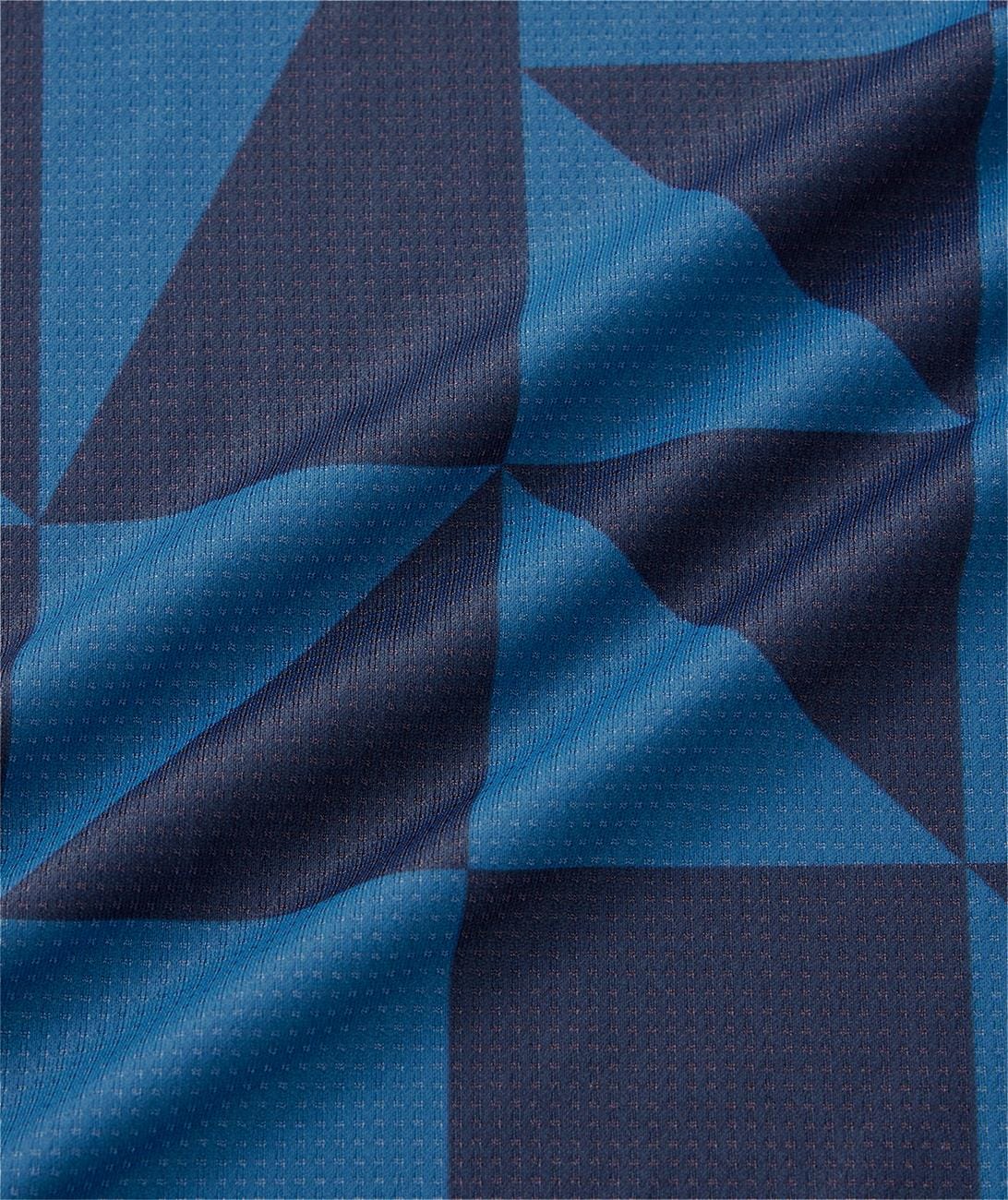 A close-up of the Yonex 10712YX Crew Neck Mens Padel T-Shirt in Indigo Blue shows textured, quick-drying sports fabric with a blue and navy geometric checkered pattern and subtle dotted details, ideal for athletic performance.