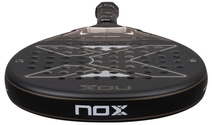 A close-up of the NOX AT10 Pro Cup Hard By Agustín Tapia 2026 padel racket, featuring a black perforated surface with the NOX logo and X-shaped design, handle angled in the background—Agustín Tapia’s top choice.