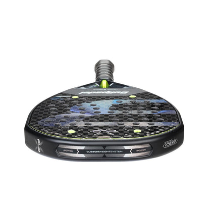 A close-up of the Bullpadel XPLO 2026 Padel Racket shows its black and blue hexagonal pattern, green accents, textured handle, and visible Bullpadel branding from the bottom.
