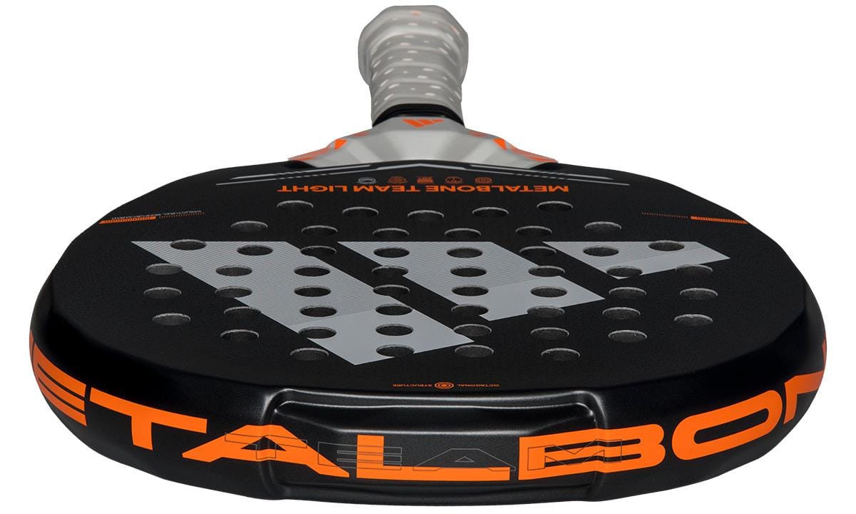 A close-up of the adidas Metalbone Team Light 2026 Padel Racket, made for advanced padel players, shows its black and orange face with perforations, "METALBONE" branding on the side, and a handle with a light-colored grip.