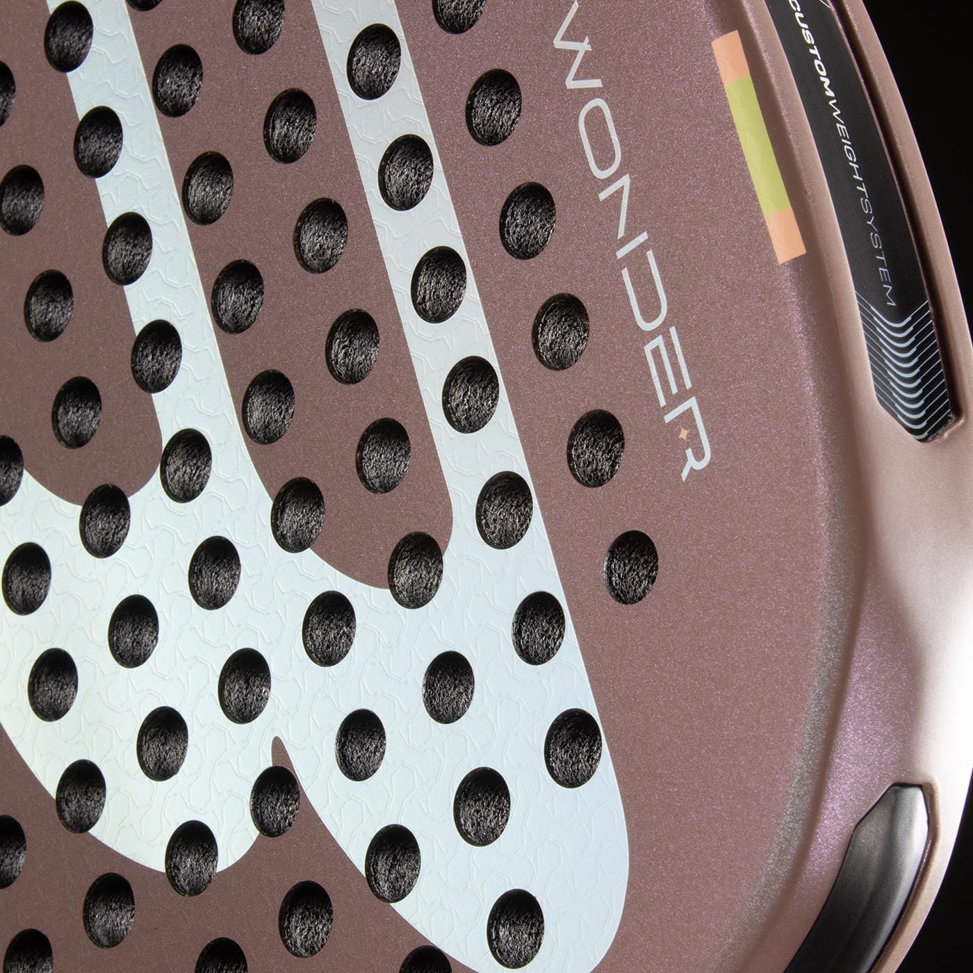 Close-up of the Bullpadel Wonder 2026 Padel Racket by Bullpadel, showcasing its textured surface with circular holes and "WONDER" printed on it. This professional racket features brown and white tones with black and yellow Hyper Core accents.
