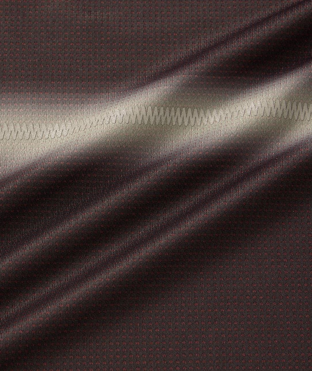 Close-up of the Yonex 10711YX Crew Neck Mens Padel T-Shirt in black, showing its dark brown textured fabric with small red dots and a zigzag seam. Light reflections highlight the surface and texture of this Yonex performance sportswear.