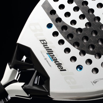 Close-up of the Bullpadel Vertex 05 2026 padel racket in white with black and grey accents, featuring the Bullpadel logo, round perforations, and a glimpse of the handle set against a black background.