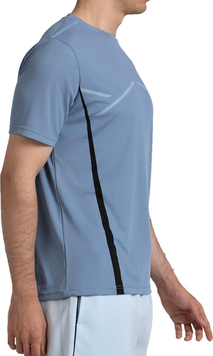 A man in profile wears a Bullpadel Cabore Men's Padel T-Shirt in Shadow Blue featuring Quickerdry tech and a black vertical stripe, paired with white athletic shorts, against a white background.