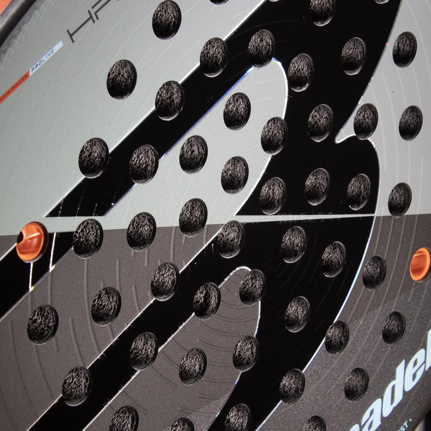 Close-up of the Bullpadel HACK 04 Comfort 2026 Padel Racket face in black and grey, featuring a textured surface with small circular holes, a bold logo, and orange edge accents that emphasize its power and control.