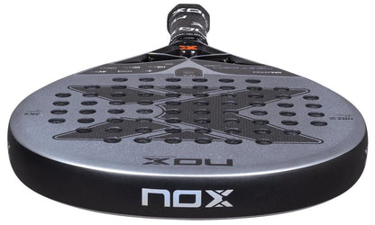 A close-up of the NOX NFA Nextgen Pro Hybrid 3K Padel Racket shows its black and silver 3K carbon surface with a large X design, circular perforations, and the NOX logo on both the edge and handle.