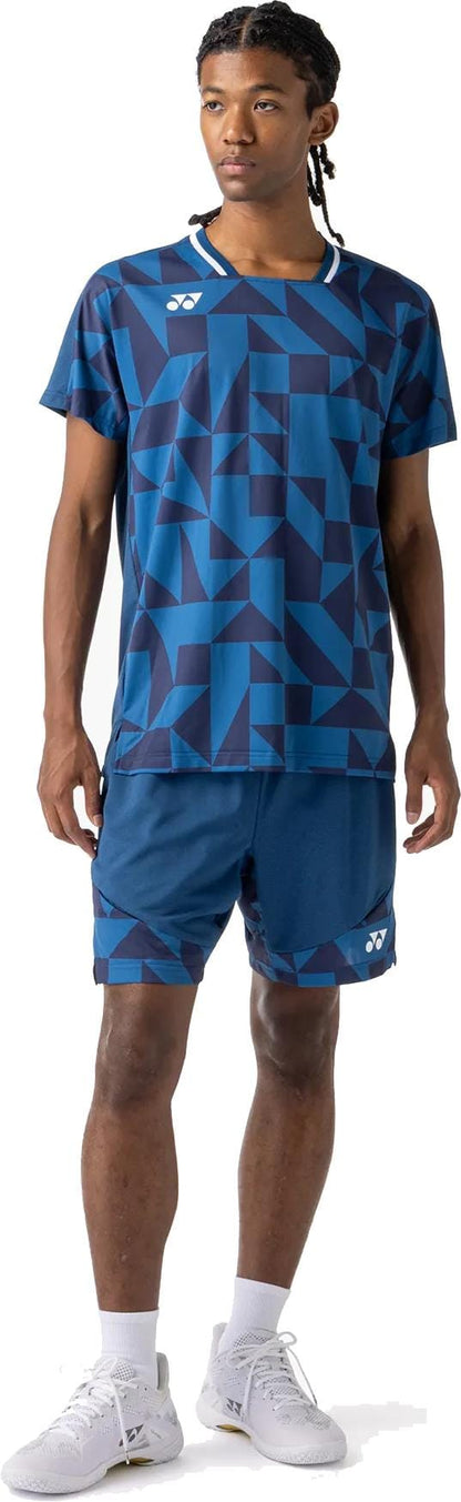 A man stands wearing the Yonex 10712YX Crew Neck Mens Padel T-Shirt in Indigo Blue, paired with matching shorts, white socks, and white athletic shoes. He looks to the side.