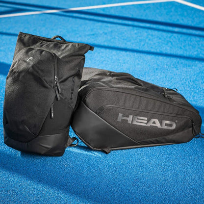 Two HEAD Pro X Padel Backpack 25L - Black by HEAD, with a racket compartment and urban style, rest on a vibrant blue outdoor court marked with white lines in the background.