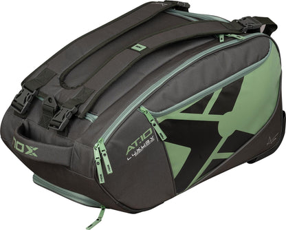 The NOX AT10 Competition Trolley Padel Racket Bag in black and green features shoulder straps, multiple zippered compartments, wheels for easy transport, and a bold stylized “X” design—ideal for padel players.