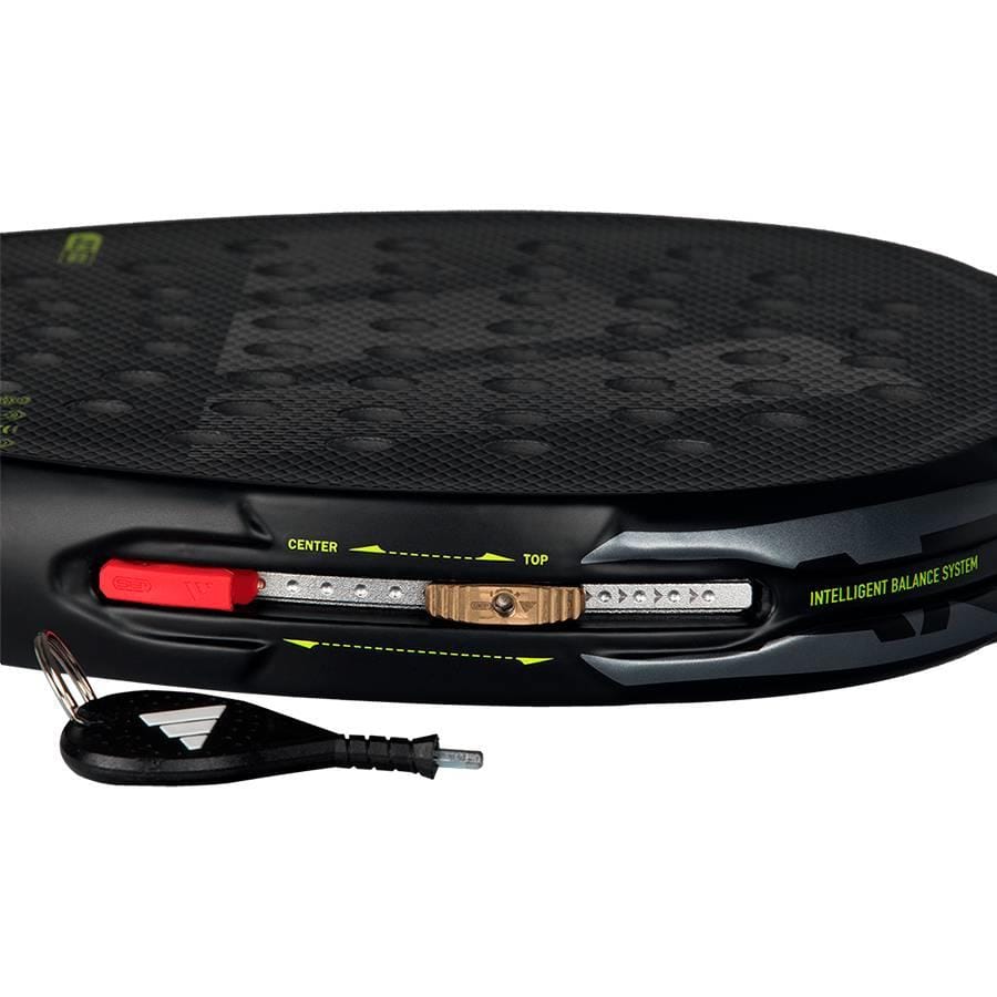 Close-up of the adidas Arrow Hit 2026 Padel Racket, showcasing its intelligent balance slider and weight indicators. A small black keychain tool is in front, emphasizing easy power and precision adjustments.