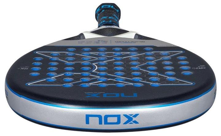 A close-up of the NOX Luxury Quantum 12K Cobalt 2025 Padel Racket, showing its round shape, blue-accented 12K carbon fibre perforated surface, and "NOX" branding on the side and face.