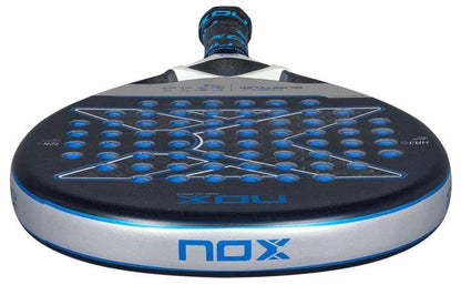 A close-up of the NOX Luxury Quantum 12K Cobalt 2025 Padel Racket, showing its round shape, blue-accented 12K carbon fibre perforated surface, and "NOX" branding on the side and face.