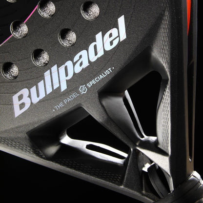Close-up of the black Bullpadel HACK 04 Comfort 2026 Padel Racket, featuring the Bullpadel logo, round perforations, and Air React Channel system for power and control. "The Padel Specialist" is seen below the logo on its geometric-cut frame.