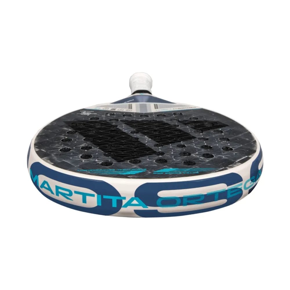 A close-up of the adidas Cross It Light 3.4 Padel Racket shows "Martita Ortega" on its white edge. The lightweight racket, pictured handle-up, displays a textured surface and large perforations.
