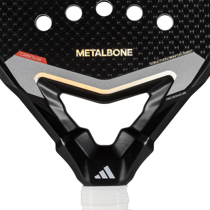Close-up of the adidas Metalbone 3.4 Padel Racket’s upper part, showing its textured surface, round holes, adidas logos, and text emphasizing carbon construction and structural reinforcement.