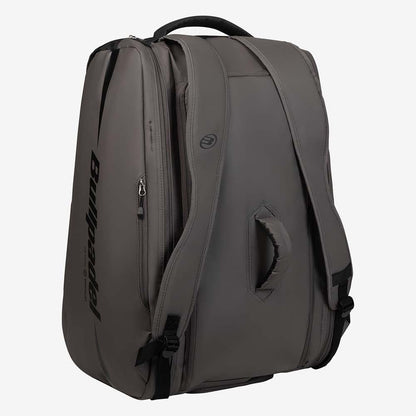 The Bullpadel BPP26022 XPLO Padel Racket Bag in grey features black straps, a padded handle, side zipper pocket, thermal racket compartments, and the Bullpadel logo on the side. The bag stands upright against a light background.
