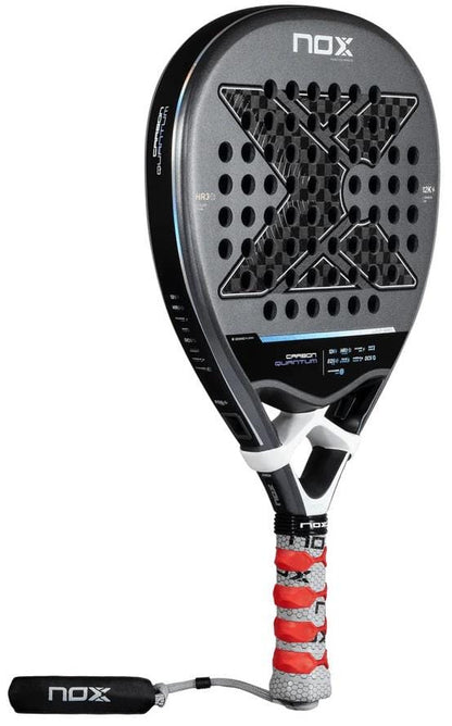 The NOX Luxury Quantum 12K Carbon 2025 Padel Racket by NOX features a black and silver design with a large X pattern, multiple round holes, 12K carbon fibre build, and a handle wrapped in red and white grip tape.
