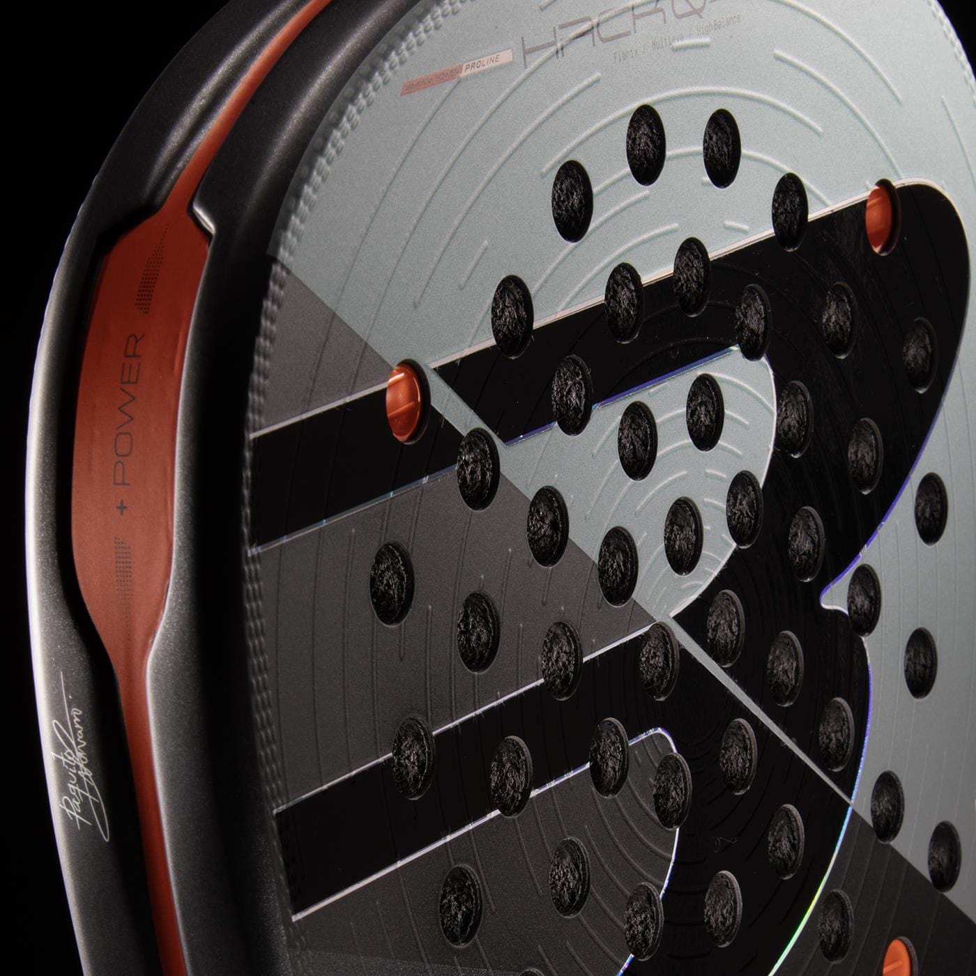 Close-up of the Bullpadel HACK 04 Comfort 2026 Padel Racket by Bullpadel, showcasing black and orange accents, a circular hole pattern, bold “S” motif, and Air React Channel system for improved power and control.