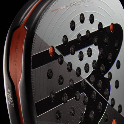 Close-up of the Bullpadel HACK 04 Comfort 2026 Padel Racket by Bullpadel, showcasing black and orange accents, a circular hole pattern, bold “S” motif, and Air React Channel system for improved power and control.