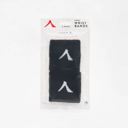 The Kanso 7cm Wristband 2 Pack offers stylish black wristbands with a white symbol, made from absorbent fabric for durability and comfort. The set comes in transparent packaging with a light gray patterned background that highlights the wristbands beautifully.