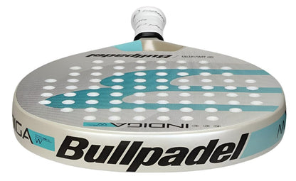 A close-up of the Bullpadel Indiga W 2025 Padel Racket displays its white, grey, and light blue design with circular perforations and Bullpadel branding on both the surface and handle.