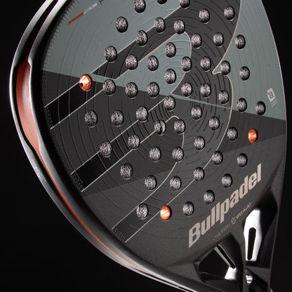 Close-up of the Bullpadel HACK 04 Comfort 2026 Padel Racket by Bullpadel, showing its black and gray design, Air React Channel system for power and control, multiple small holes, and silver-orange accents on a black background.