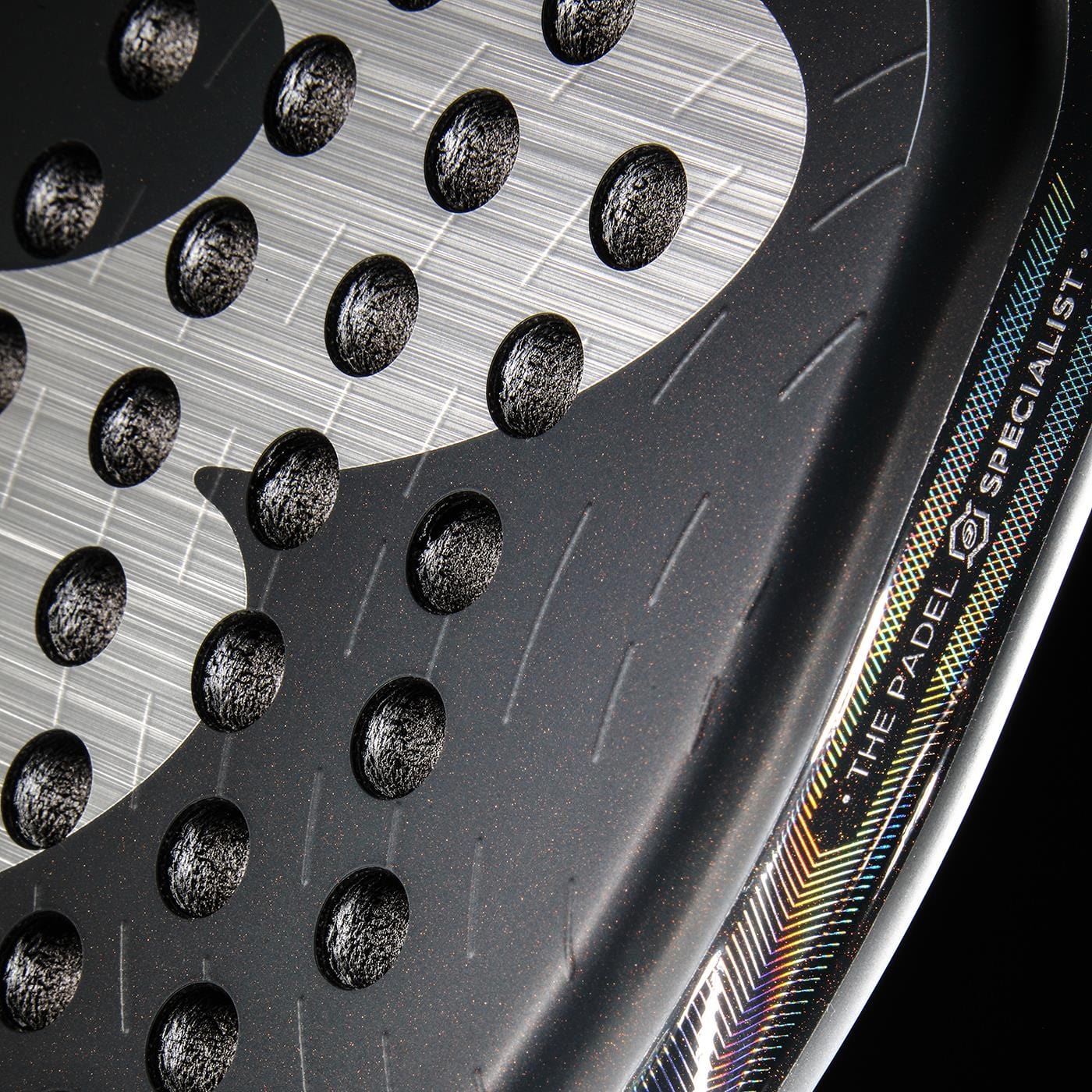 Close-up of the Bullpadel XPLO Comfort 2026 Padel Racket face, featuring circular holes, a textured surface, and part of a colorful border with “THE PADEL SPECIALIST” on the edge; designed for explosive power and comfort.