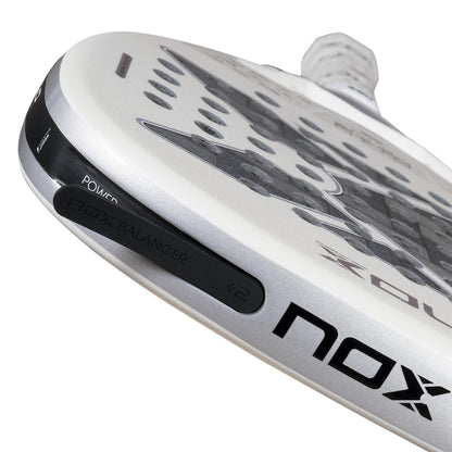 Close-up of the NOX AT10 Genius Attack 12K Alum Extrem By Agustín Tapia 2026 padel racket, showing "NOX BALANCER +2," "POWER," and the NOX brand. The sleek white-silver design reflects its focus on precision and power for enthusiasts.