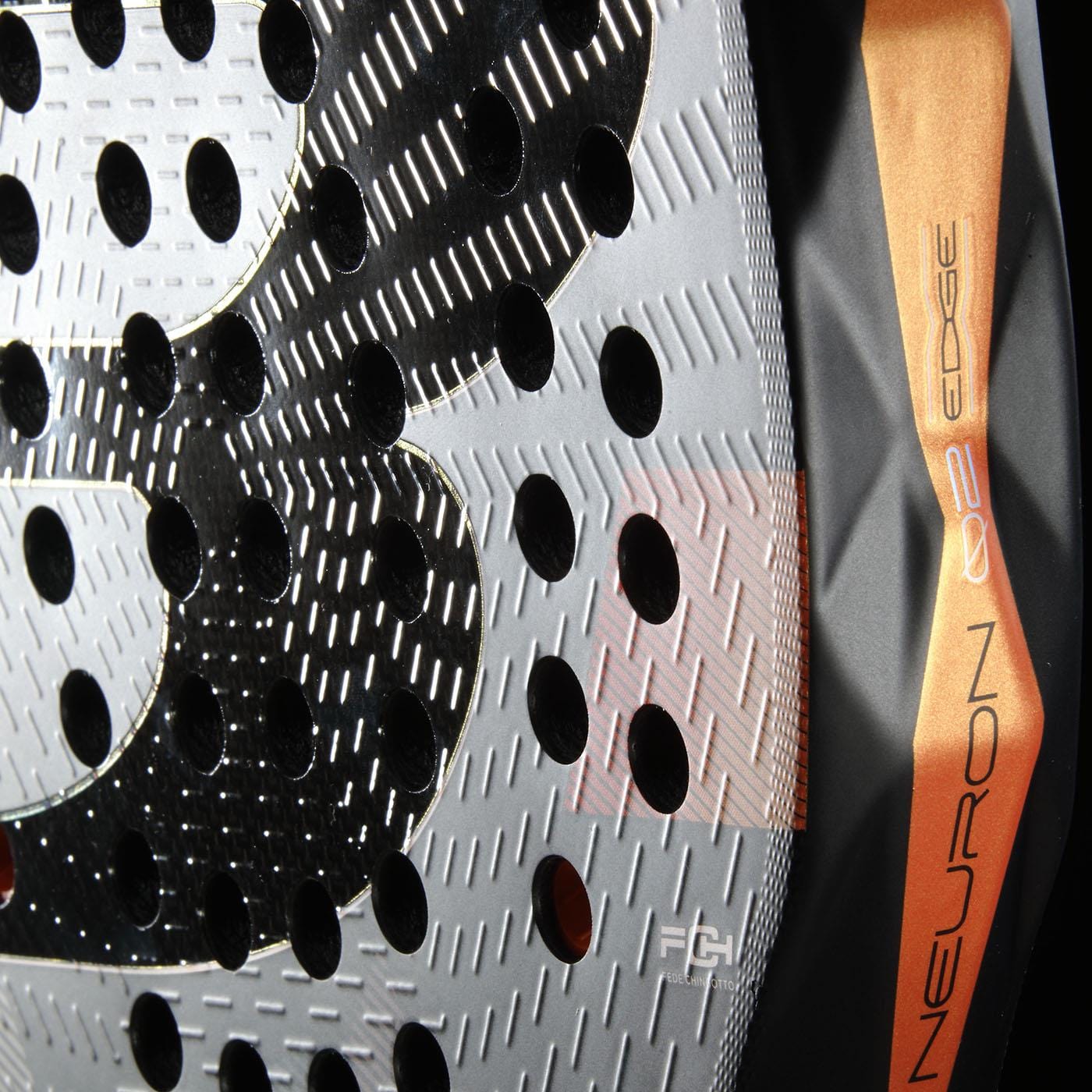 Close-up of the Bullpadel Neuron 02 Edge 2026 Padel Racket, featuring a perforated metallic surface with textured patterns, a bold black "B," and an orange edge labeled "NEURON 02 EDGE" with PrismLock technology.