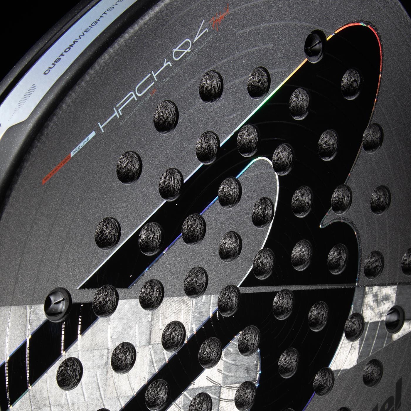 Close-up of the Bullpadel HACK 04 Hybrid 2026 Padel Racket with circular perforations, striking silver and black design, "HACK 04" text, and textured details highlighted by light reflections. Features innovative Total Channel technology.