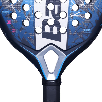 Close-up of the Babolat Air Veron 2.5 padel racket in blue and black, featuring a geometric design, round holes, and a triangular opening above the grip. The word "CARBON" highlights dynamic power alongside bold Babolat branding.