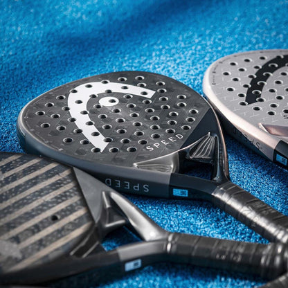 Three black and gray HEAD Speed Pro 2025 Padel Rackets with Power Foam and Auxetic 2.0 technology lie on a blue textured court, with "SPEED" branding visible on two of the rackets.