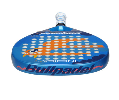 The Bullpadel Indiga Junior 25 Boys padel racket in blue with orange and white accents, "INDIGA" on its surface, and circular perforations is shown with the handle facing upward.