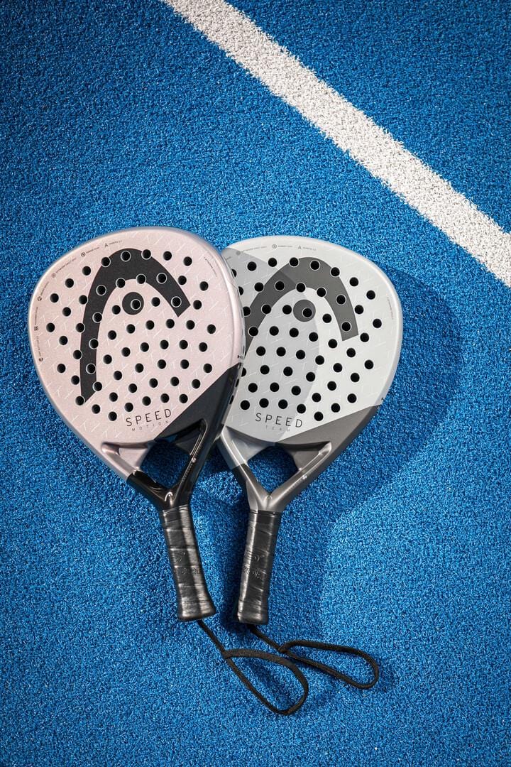 Two HEAD Speed Team 2025 Padel Rackets by HEAD, one pink and one gray with black handles and featuring Auxetic 2.0 technology for power and control, are side by side on a blue court near a white line.