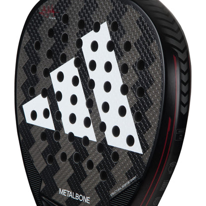 Close-up of the adidas Metalbone 3.3 Padel Racket, featuring a textured carbon fiber surface, circular perforations, white adidas logo, red accents, and adjustable weight design with tread-like edge patterns.
