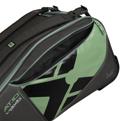 Close-up of the NOX AT10 Competition Trolley Padel Racket Bag by NOX in black and green, featuring a bold graphic, "AT10 Luxury" branding, wheels for easy transport, and a spacious zippered compartment partially open.