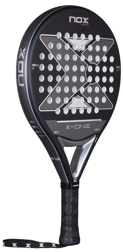The NOX X-One Advance Series Padel Racket in black features silver and white detailing, a perforated surface, HR3 rubber core, large central X design, and a black grip with NOX branding on the neck and handle.