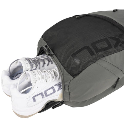 A pair of white NOX sneakers peeks from the NOX Street Series Padel Backpack - Grey, featuring ergonomic padded straps and a mesh zippered compartment. The visible NOX logo on both makes it ideal for your sports adventures.