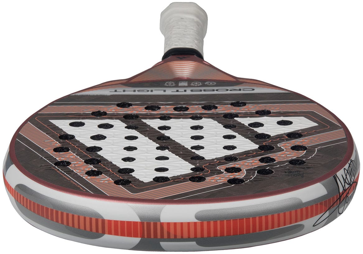 Close-up of the adidas Cross It Light 2026 Padel Racket, featuring a white handle and a red, black, and gray carbon fibre geometric design with multiple holes in a triangular pattern on the hitting surface.