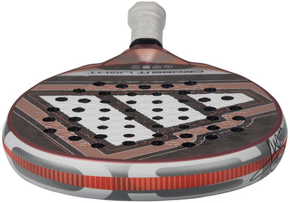 Close-up of the adidas Cross It Light 2026 Padel Racket, featuring a white handle and a red, black, and gray carbon fibre geometric design with multiple holes in a triangular pattern on the hitting surface.