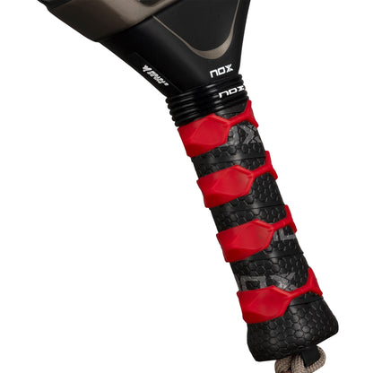 Close-up of the black and red textured grip on the handle of the NOX AT10 Pro Cup Hard By Agustín Tapia 2026 Padel Racket, featuring a gray wrist strap.
