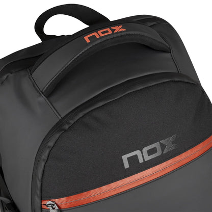 Close-up of the NOX Luxury Open Series Padel Backpack in black/red, featuring "nox" branding in gray and orange on the front pocket and handle, an orange zipper accent, and a smooth, slightly shiny material.