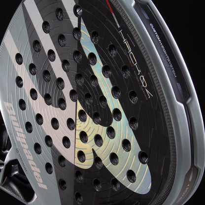 Close-up of the black and silver Bullpadel HACK 04 2026 padel racket, highlighting its perforated surface, textured details, and Bullpadel branding, with "HACK 04" and "Custom Weight System" visible on the top edge.
