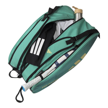 The ADIDAS Control 3.4 Padel Racket Bag - Green is open, revealing a tennis racket, a wooden-capped water bottle, and a black and white sports towel. Designed for court accessories, it features multiple compartments and a comfortable shoulder strap.