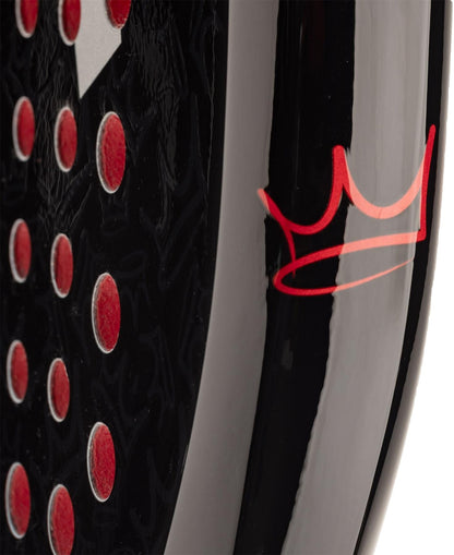 Close-up of the HEAD Coello Team 2025 Padel Racket by HEAD, showing its black surface with red circular holes and a red crown logo, featuring Auxetic 2.0 technology for superior sports performance.